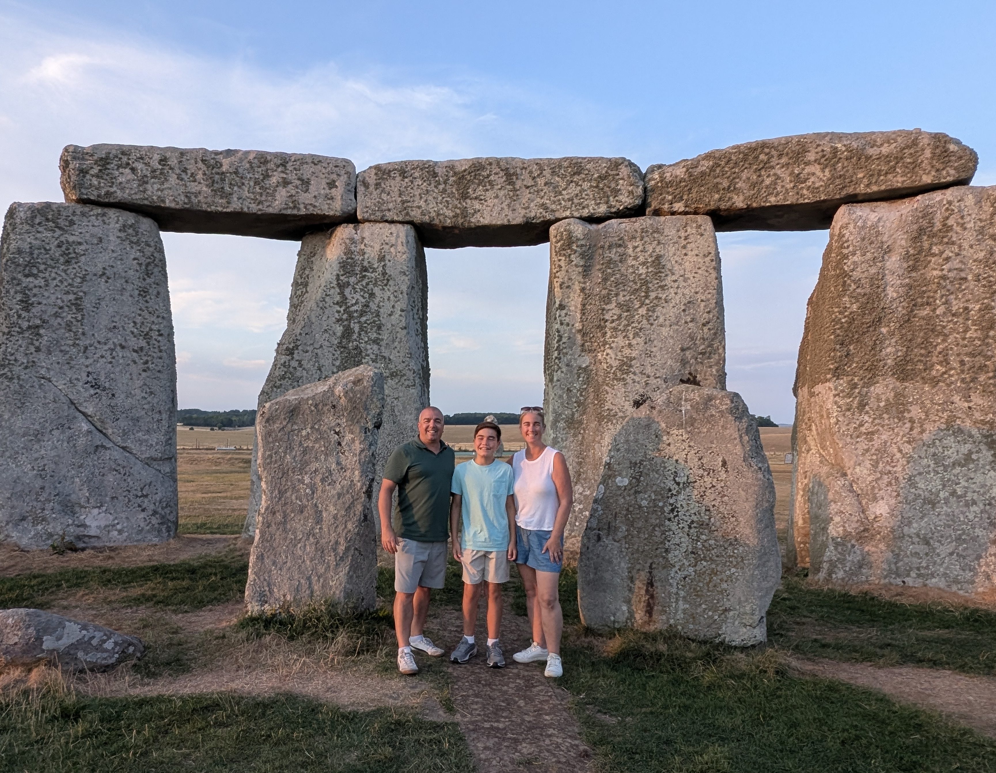 A family stands in front of Stonehenge, a prehistoric monument made of large stone blocks, during sunset.